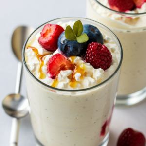 A delectable cottage cheese smoothie, featuring a blend of creamy white cottage cheese topped with fresh berries and a drizzle of honey. The smoothie is served in a clear, tall glass, accompanied by a spoon and a straw. The overall presentation is inviting and refreshing, perfect for a healthy and satisfying snack or breakfast option.