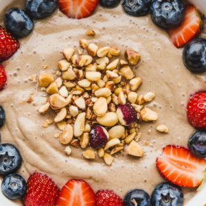 A close-up, overhead shot of a smoothie bowl featuring a creamy base, vibrant fresh fruit like strawberries and blueberries, and crunchy nuts scattered on top. The bowl look vibrant, colorful, and mouth-watering.